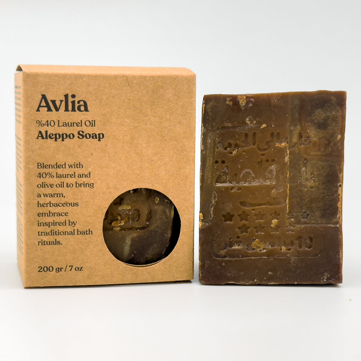 A comparison shot showing the Avlia cardboard packaging box standing next to the unwrapped Aleppo soap bar