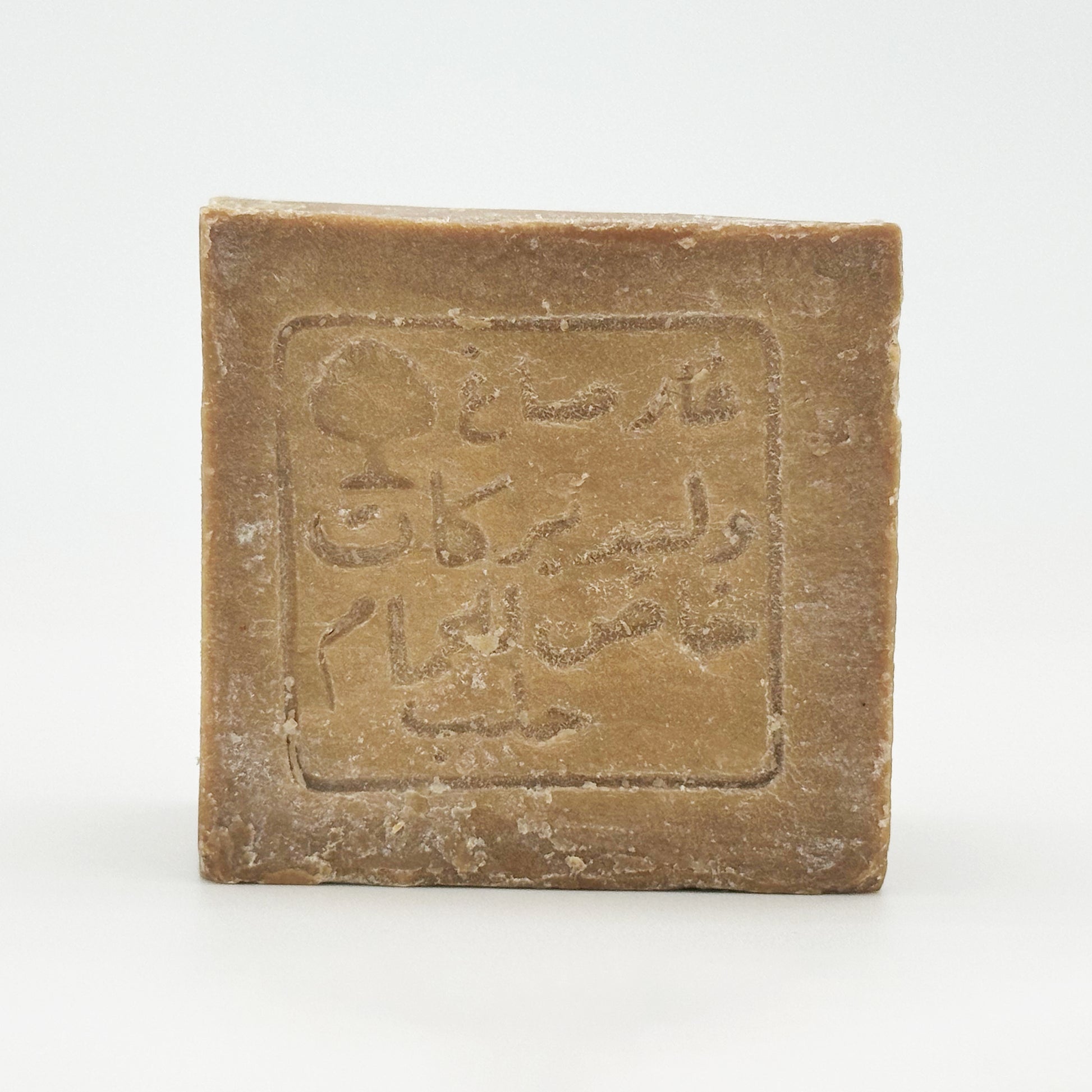 A sharp, frontal close-up of a single Aleppo soap bar, clearly displaying the intricate traditional Arabic seal stamped into the center of the textured brown surface