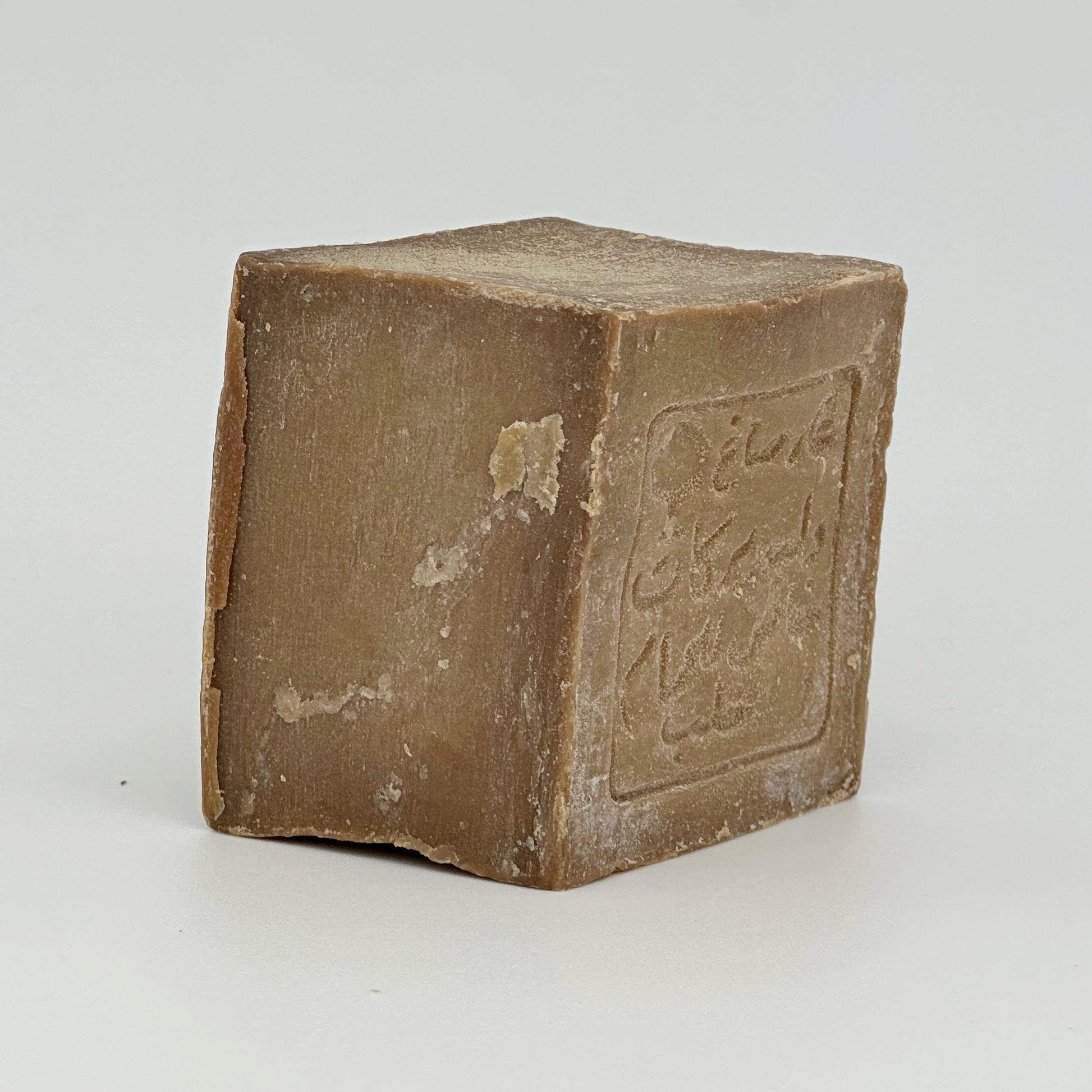 A side profile of the Aleppo soap bar, emphasizing its thick, cubic shape and the slight color variations on the surface caused by the long aging and drying process