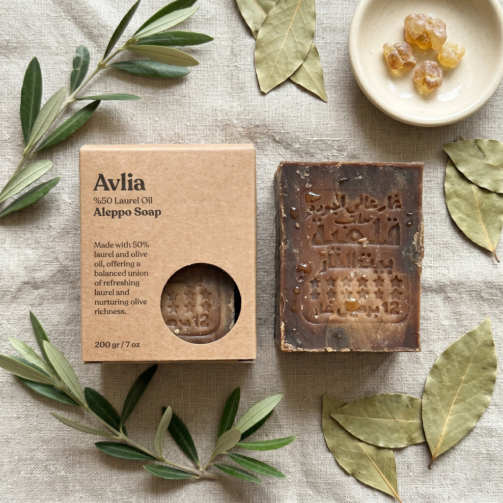 Avlia 50% Laurel Oil Aleppo Soap and kraft box overhead flat lay with olive branches and bay laurel leaves on linen, natural handmade soap product photography