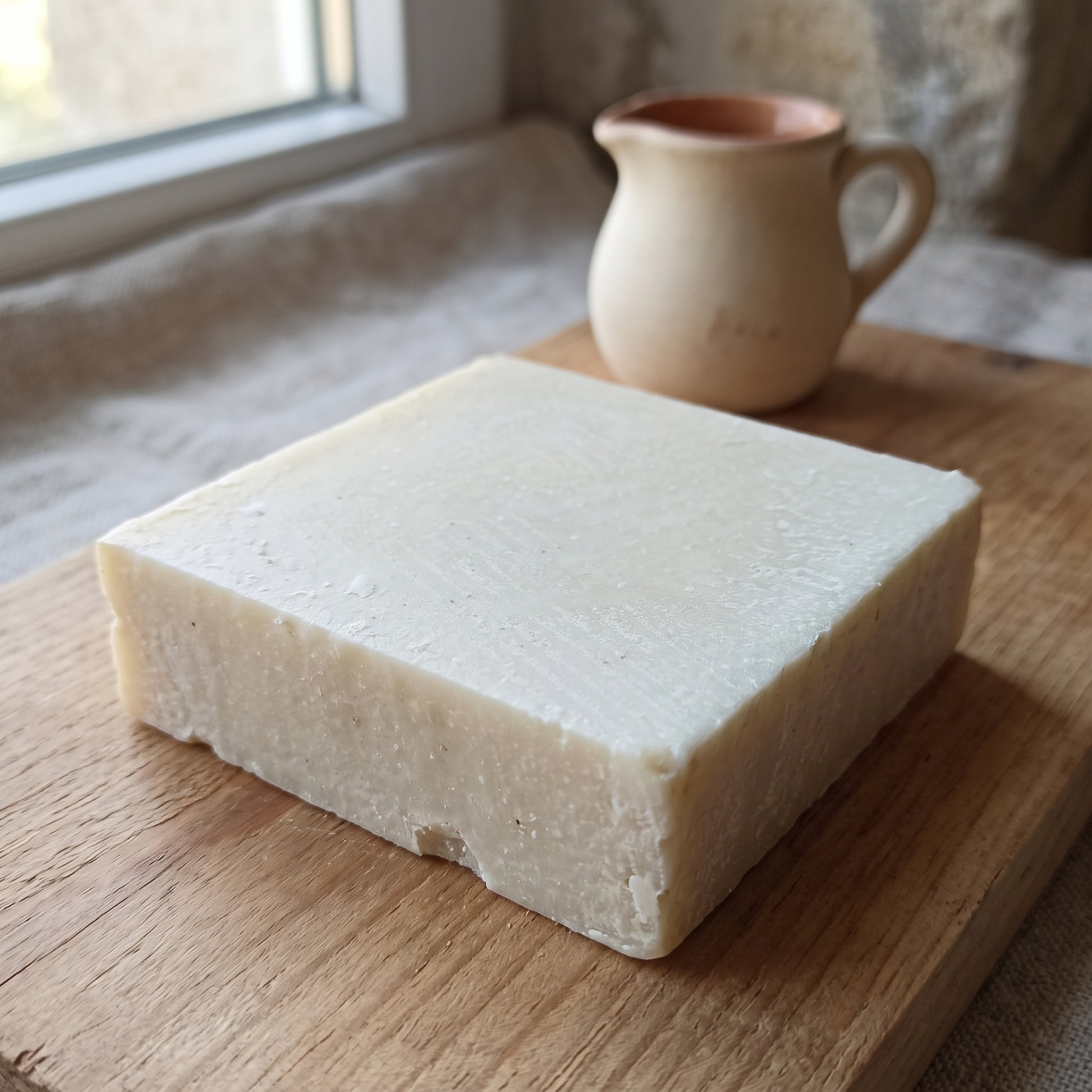 Avlia Donkey Milk Soap block on raw wood with a small ceramic milk pitcher, soft morning light.