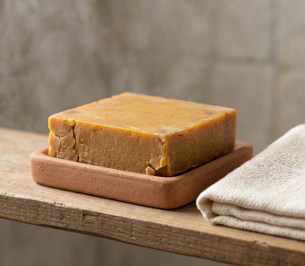 Avlia Pure Sulfur Soap on a ceramic dish beside a folded peshtemal towel, bathroom shelf styling.