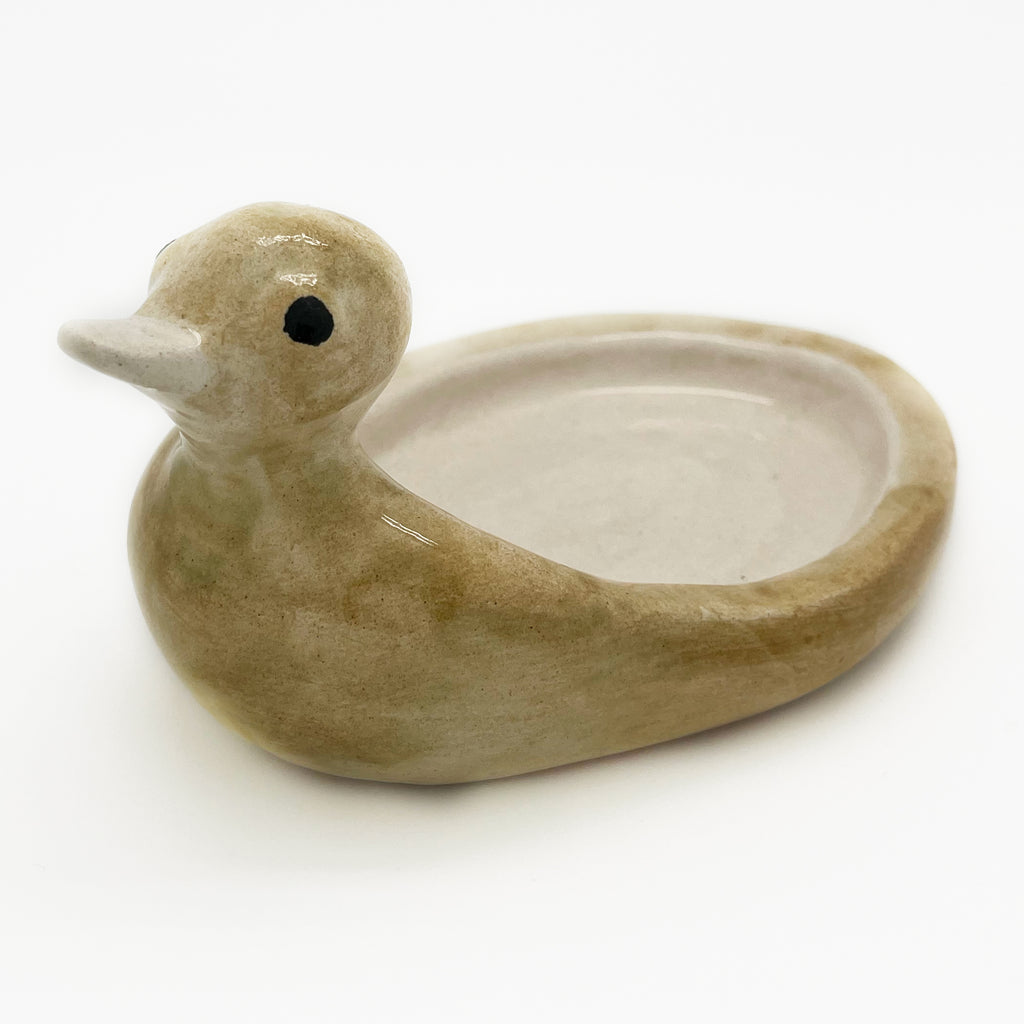 Avlia ceramic duck soap dish in pale cream glaze, three-quarter view showing the same form as the green-mustard pieces in a lighter tone