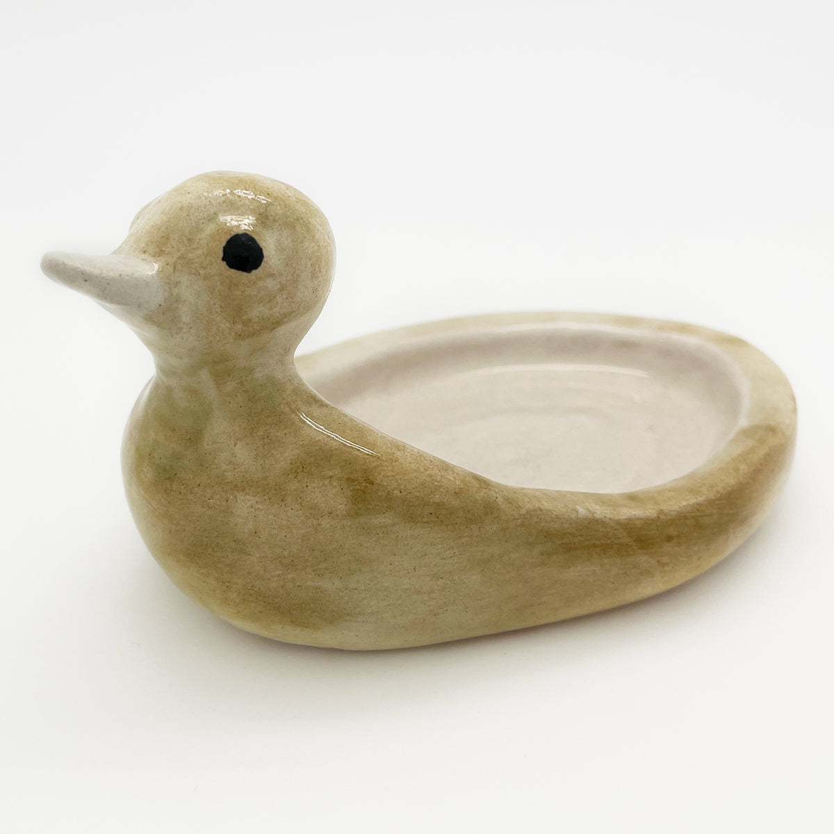 Avlia ceramic duck soap dish in pale cream, three-quarter view with the cream bowl interior and the single black eye dot both visible