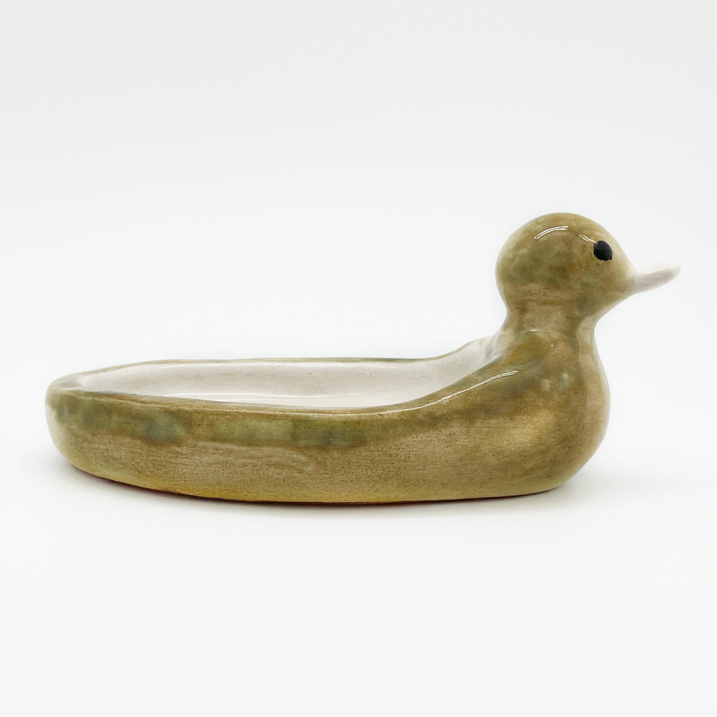 Avlia ceramic duck soap dish photographed at eye level from the right, showing how shallow the hollowed bowl sits between the raised breast and tail