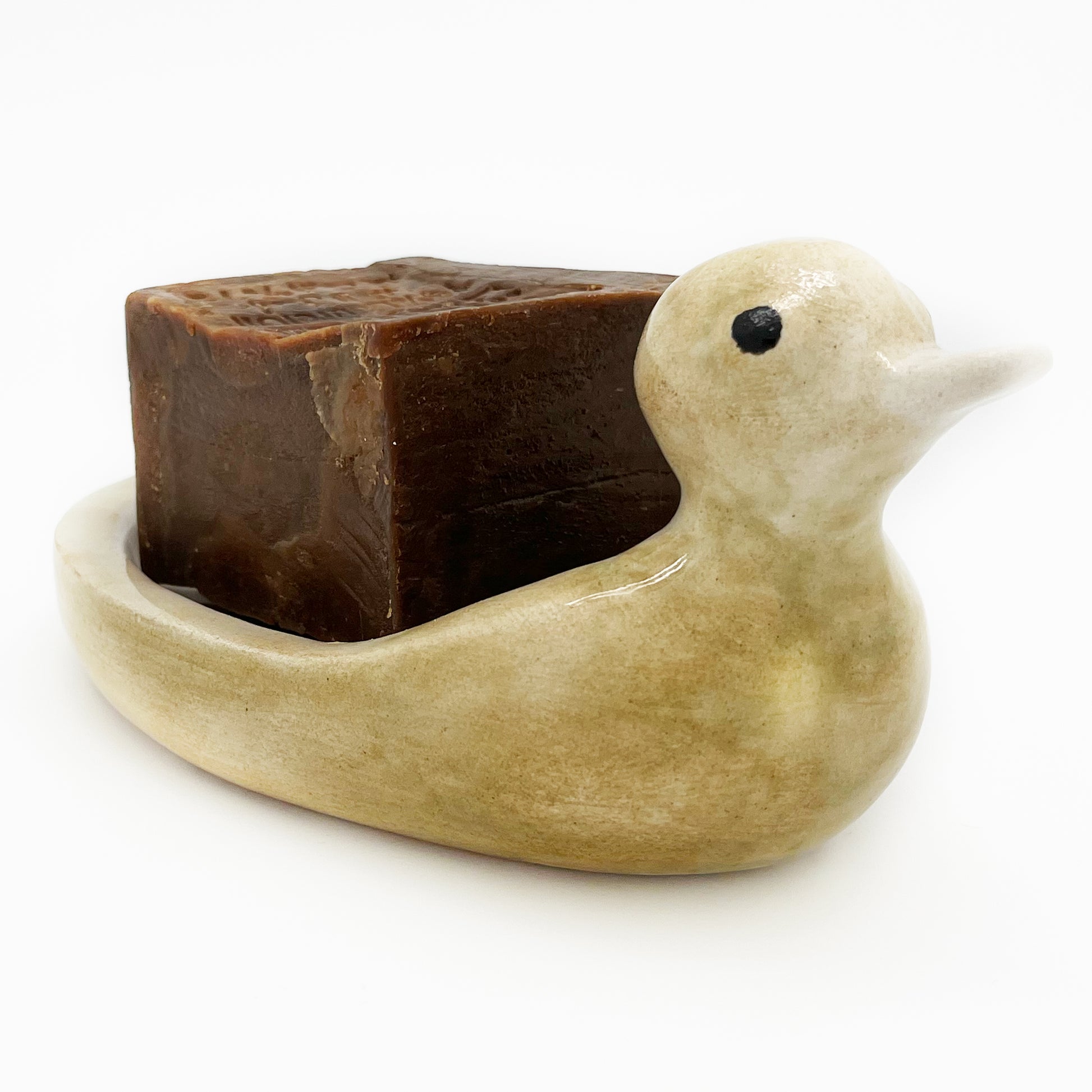 Avlia ceramic duck soap dish with a dark bar of Aleppo soap set in the bowl, photographed against white with the beak turned to the right
