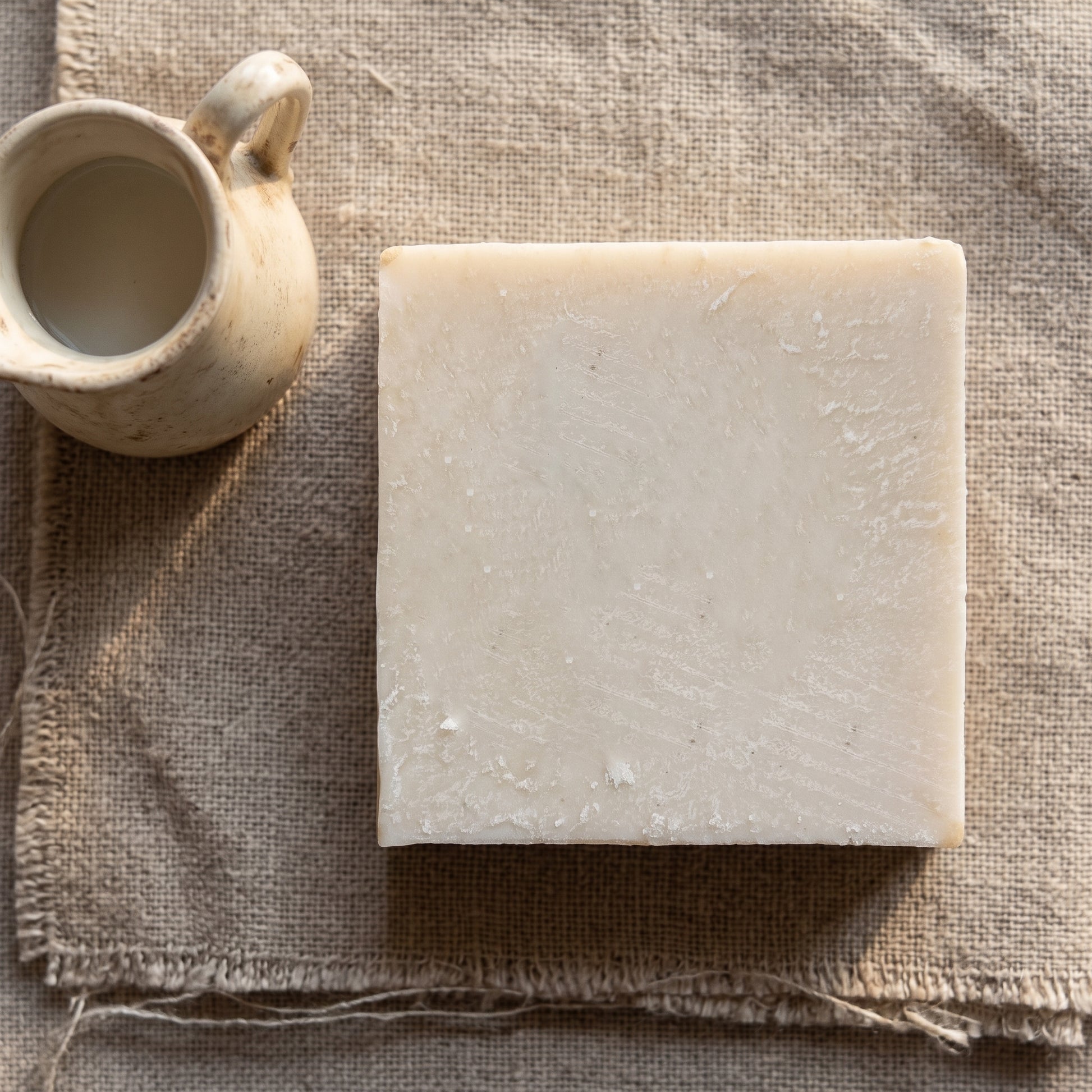 Avlia donkey milk soap with a small ceramic milk jug on linen, ingredient story flatlay.