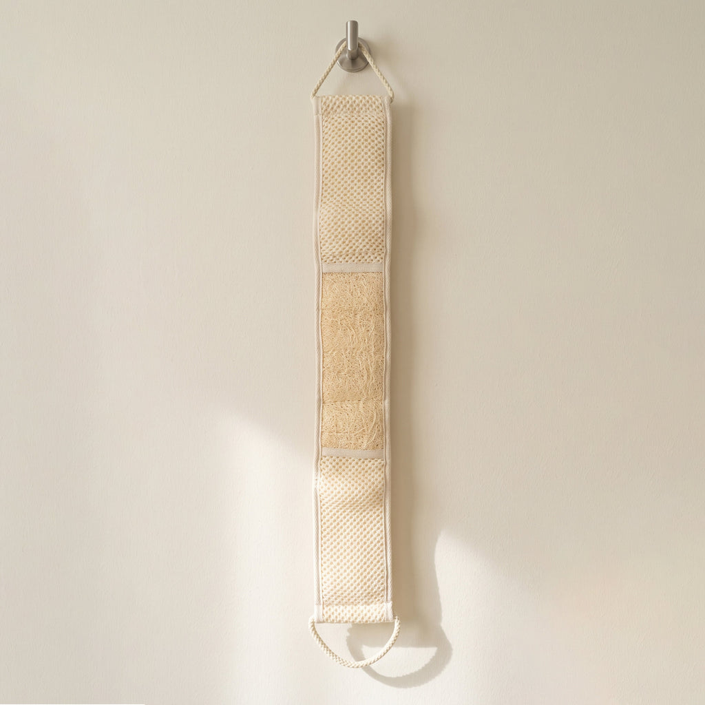 Avlia extra long loofah back strap hanging its full length from a hook on a pale wall, all three zones of the working face visible