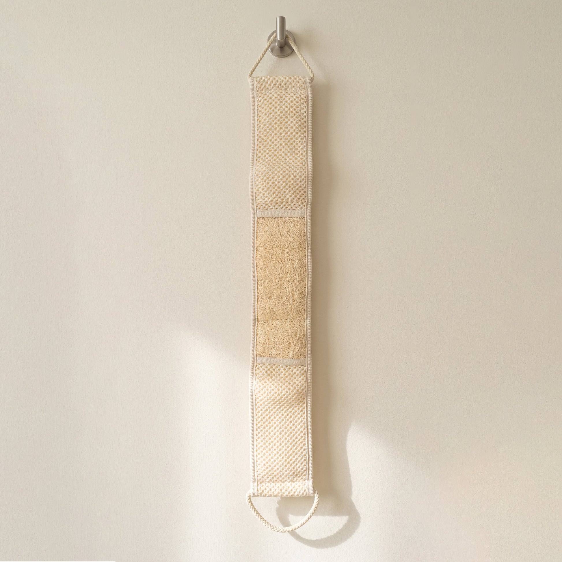 Avlia extra long loofah back strap hanging its full length from a hook on a pale wall, all three zones of the working face visible