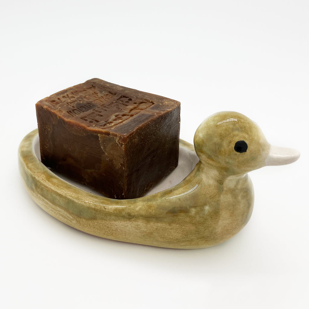 Avlia ceramic duck soap dish holding a bar of traditional Aleppo soap, showing how a full-size 200 g bar sits in the hollowed back with room to spare