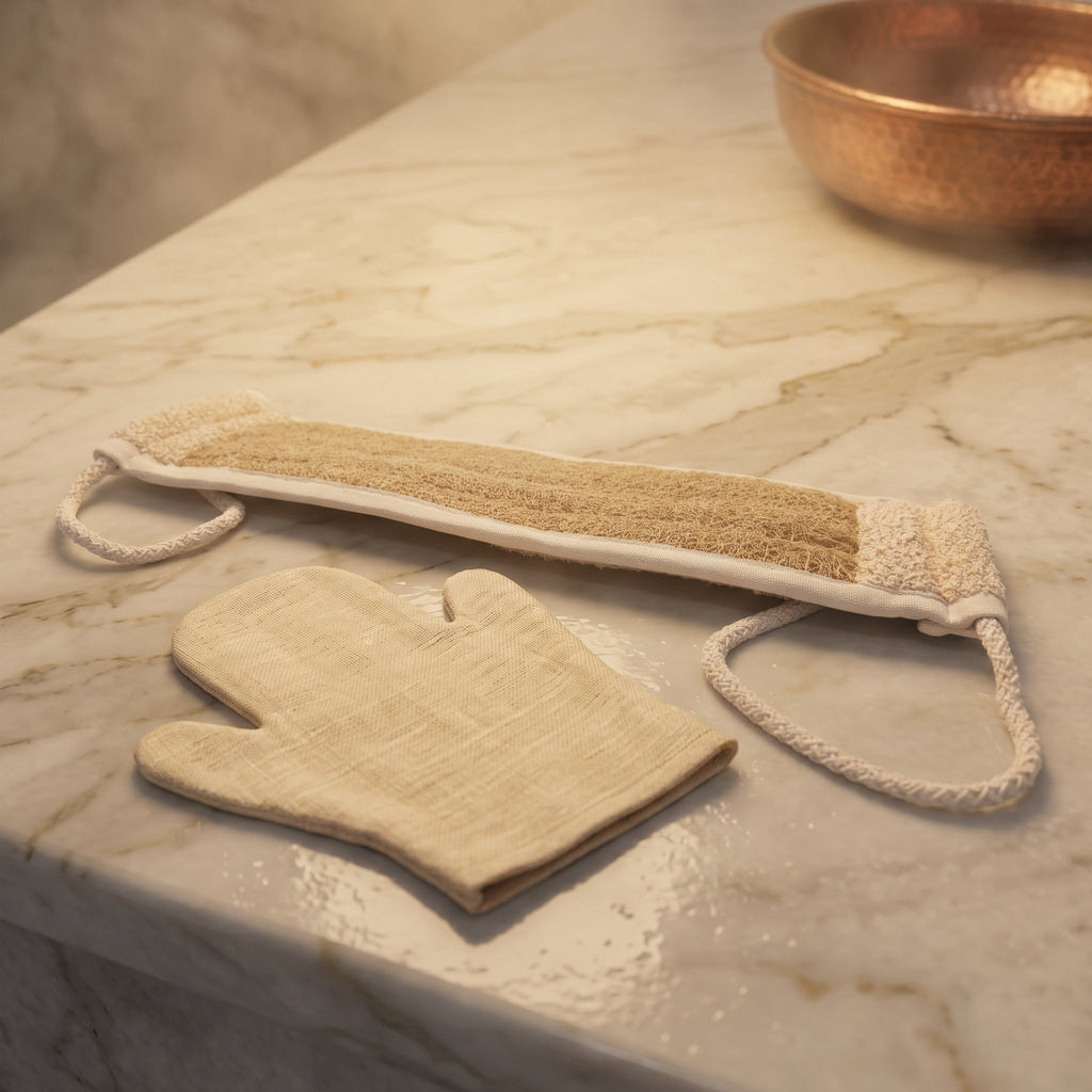 Avlia luffa back strap laid beside a traditional Turkish kese mitt on pale marble, showing clearly that the two are different bath tools
