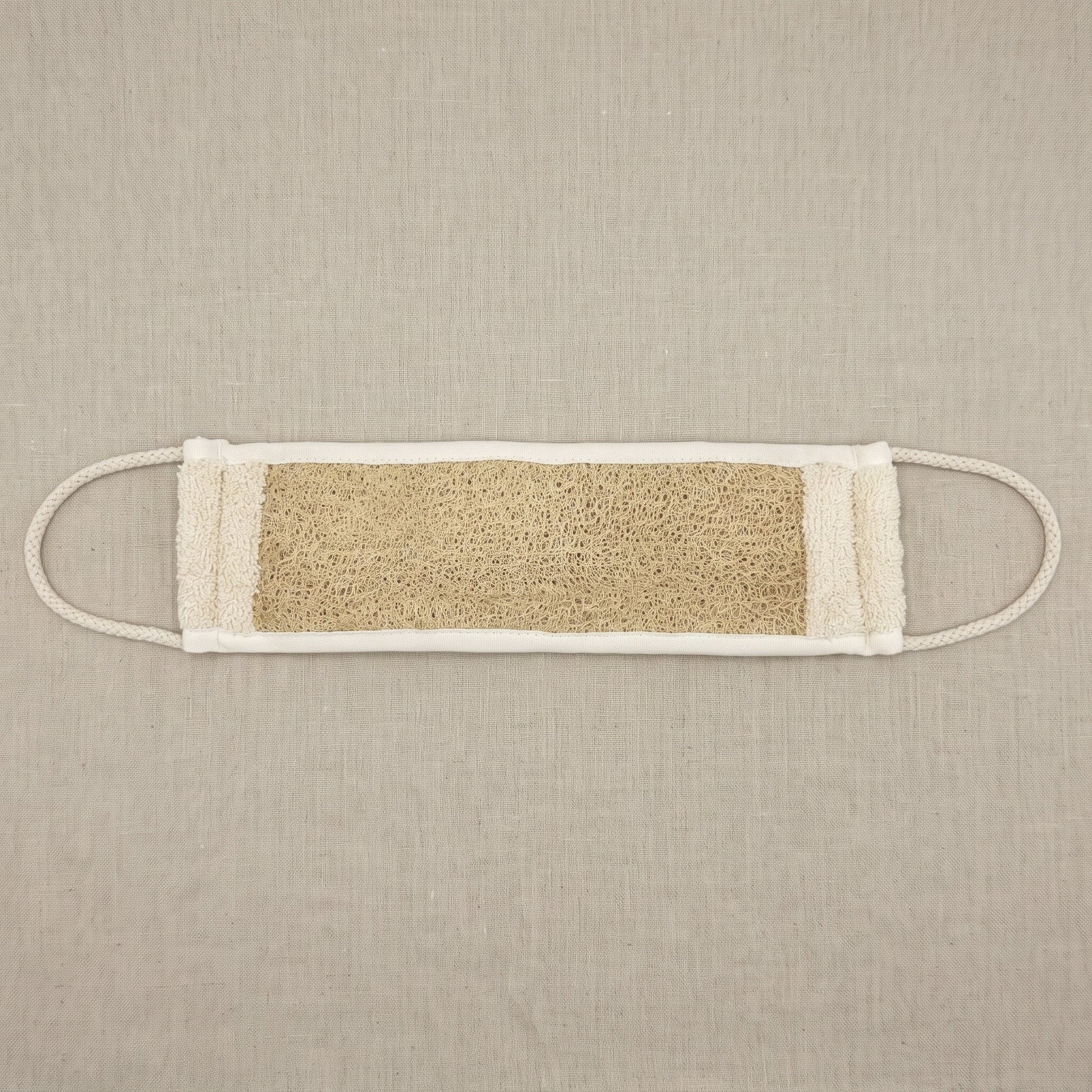Avlia natural luffa back strap laid flat on linen, fully extended to its full length with a braided cotton loop stretched out at each short end