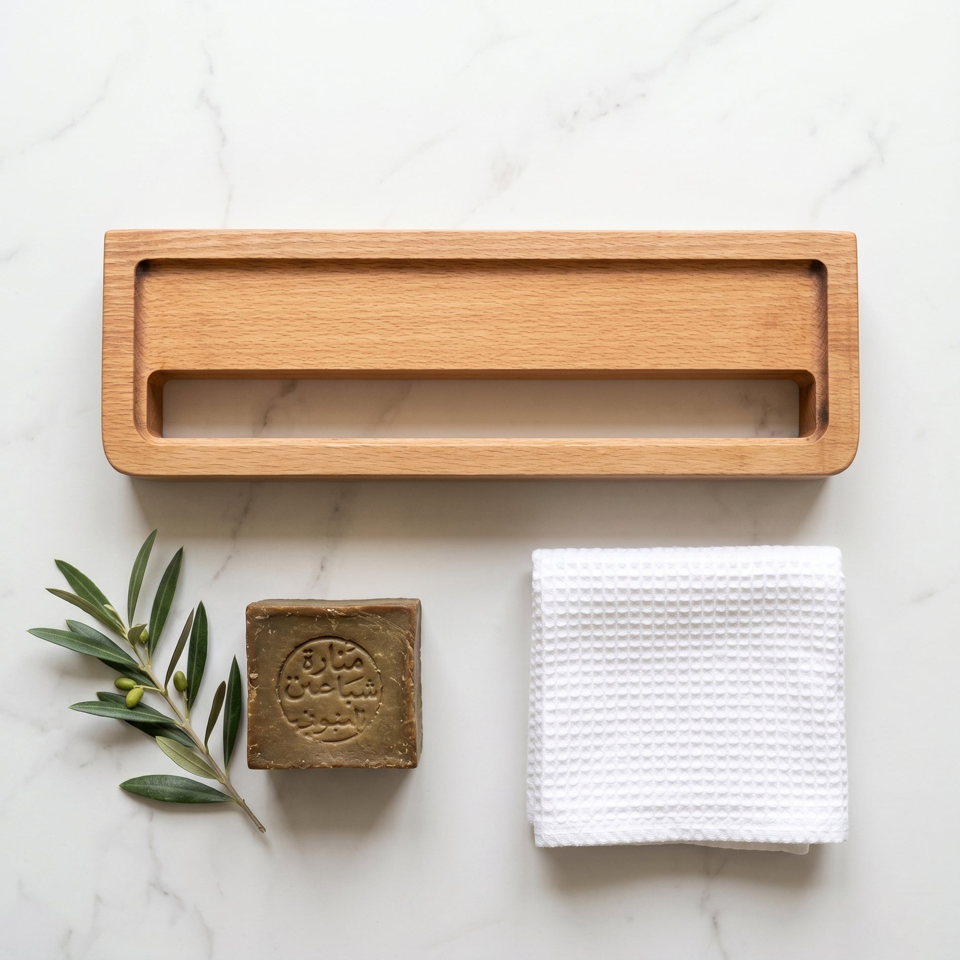 Avlia beechwood towel shelf flat lay with Aleppo soap bar, folded white towel, and olive branch on white marble, natural bathroom accessories collection