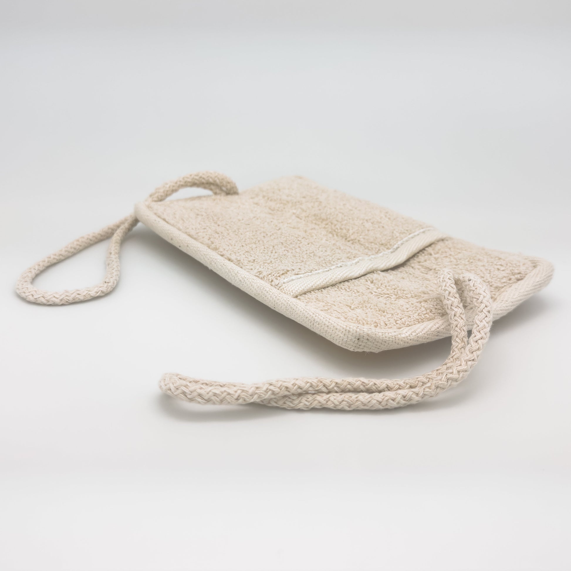 Avlia loofah bath pad back side laid flat, hand pocket clearly visible in the terry face with a braided cotton cord at each short end