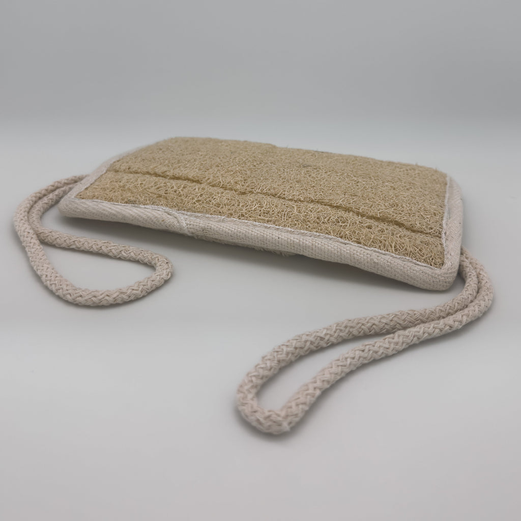 Avlia loofah bath pad with both braided cotton cords extended, rectangular pad held two-handed for back exfoliation