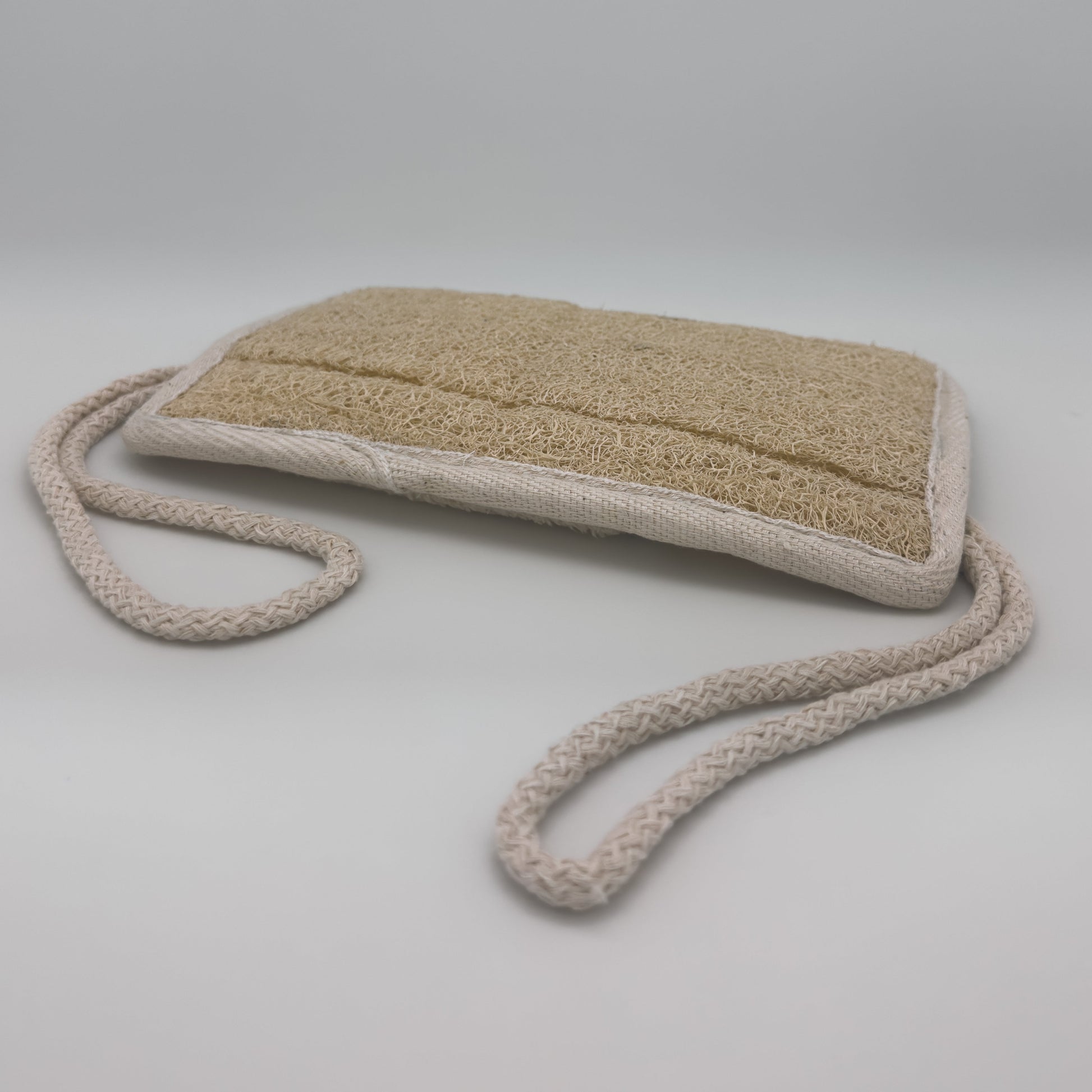 Avlia loofah bath pad with both braided cotton cords extended, rectangular pad held two-handed for back exfoliation