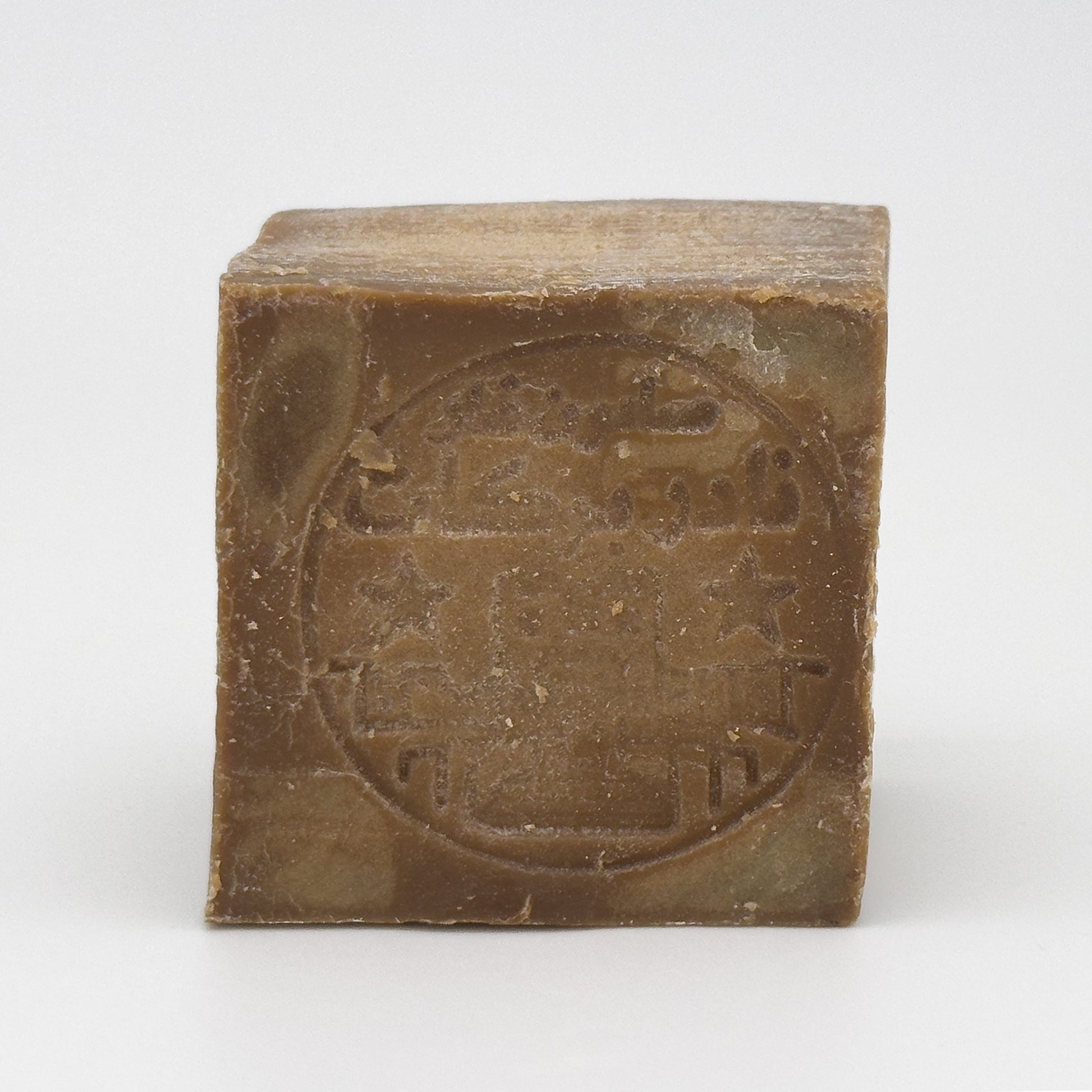 Close-up front view of a square Aleppo soap bar featuring a circular impressed logo with stars and Arabic calligraphy