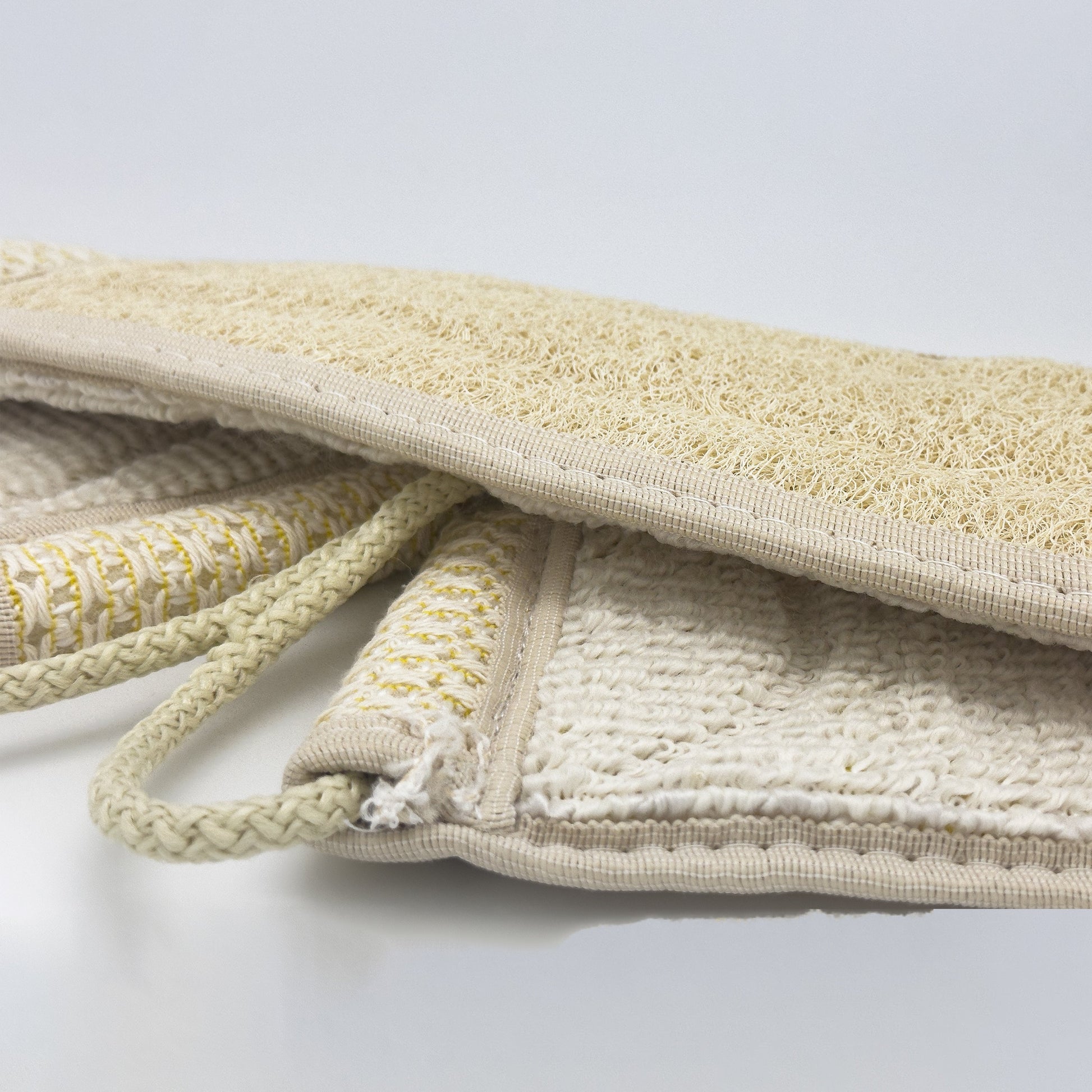 Close-up of the Avlia back strap edge showing the loofah panel, the waffle-knit cotton zone beside it and the cream terry reverse face underneath
