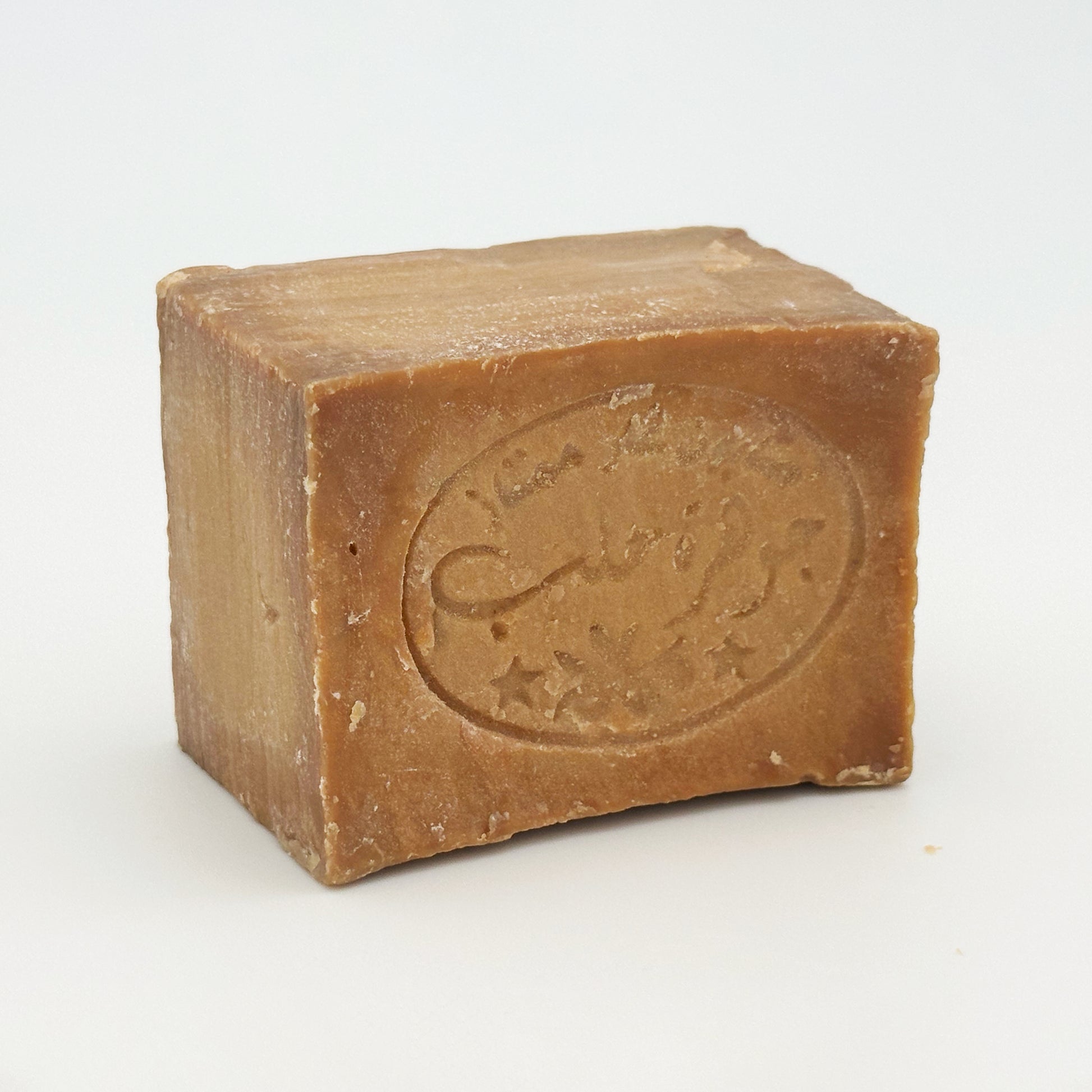 Close-up angled view of Avlia Aleppo soap bar featuring stamped Arabic calligraphy and natural golden-brown color