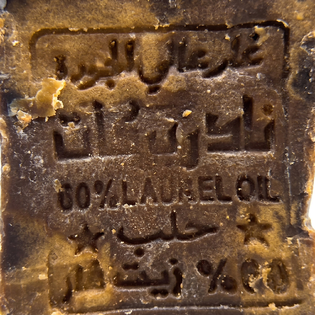 Extreme close-up of traditional Arabic stamp impression on Avlia 60% Laurel Oil Aleppo Soap surface, centuries-old hand-pressed production seal on handmade dark brown bar