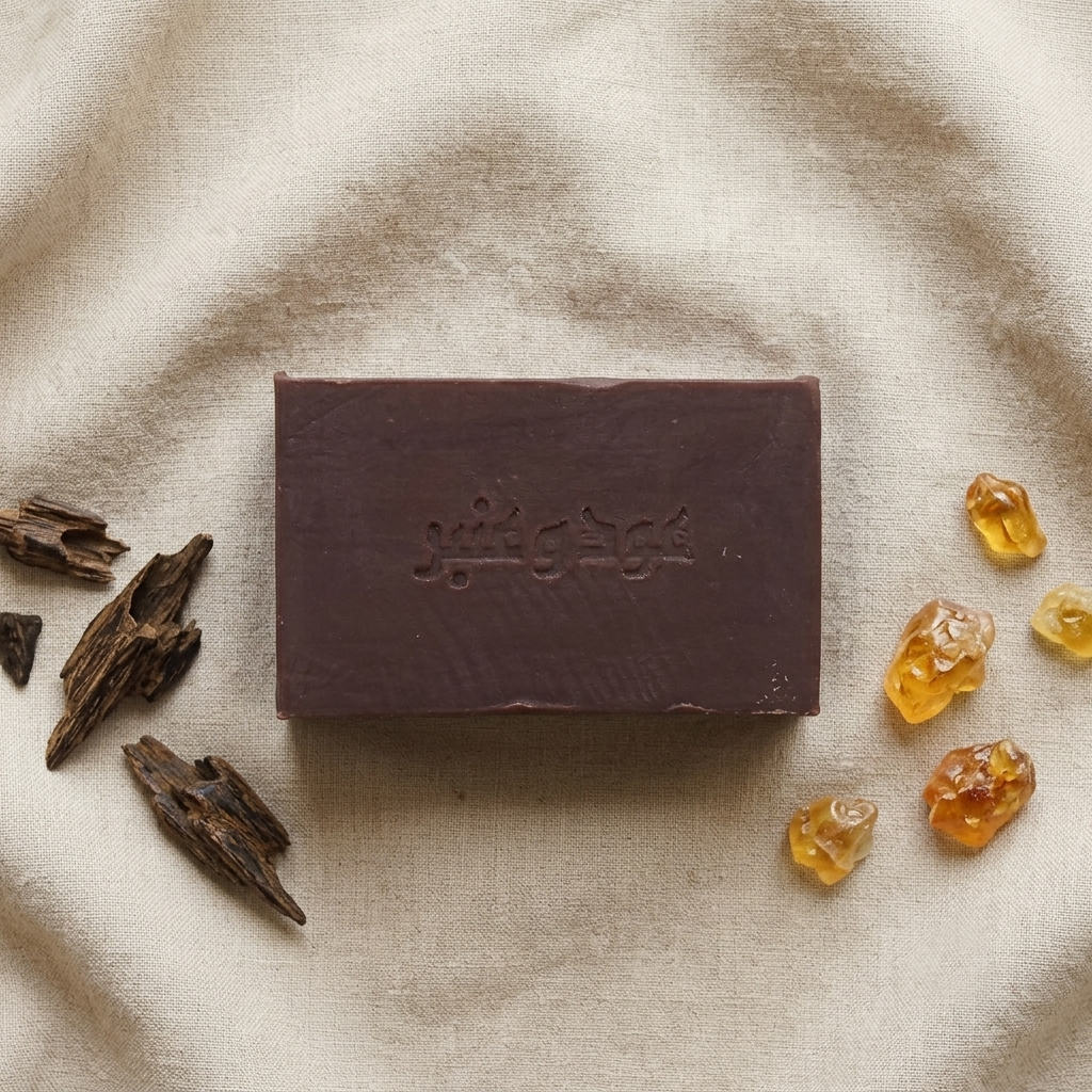 Flat lay of Avlia Oud & Anbar soap on linen with agarwood chips and golden amber resin — natural soap perfumed with royal oud and amber.