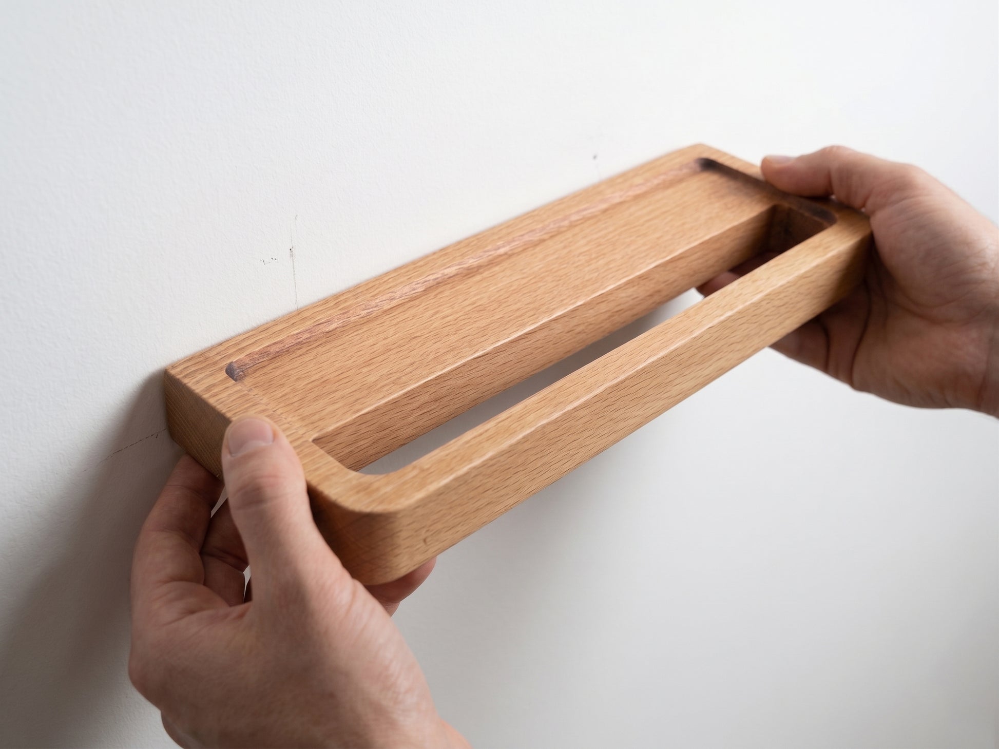 Hands installing Avlia beechwood towel shelf on bathroom wall, narrow back edge aligned with keyhole screws, shelf projecting outward, easy DIY mounting