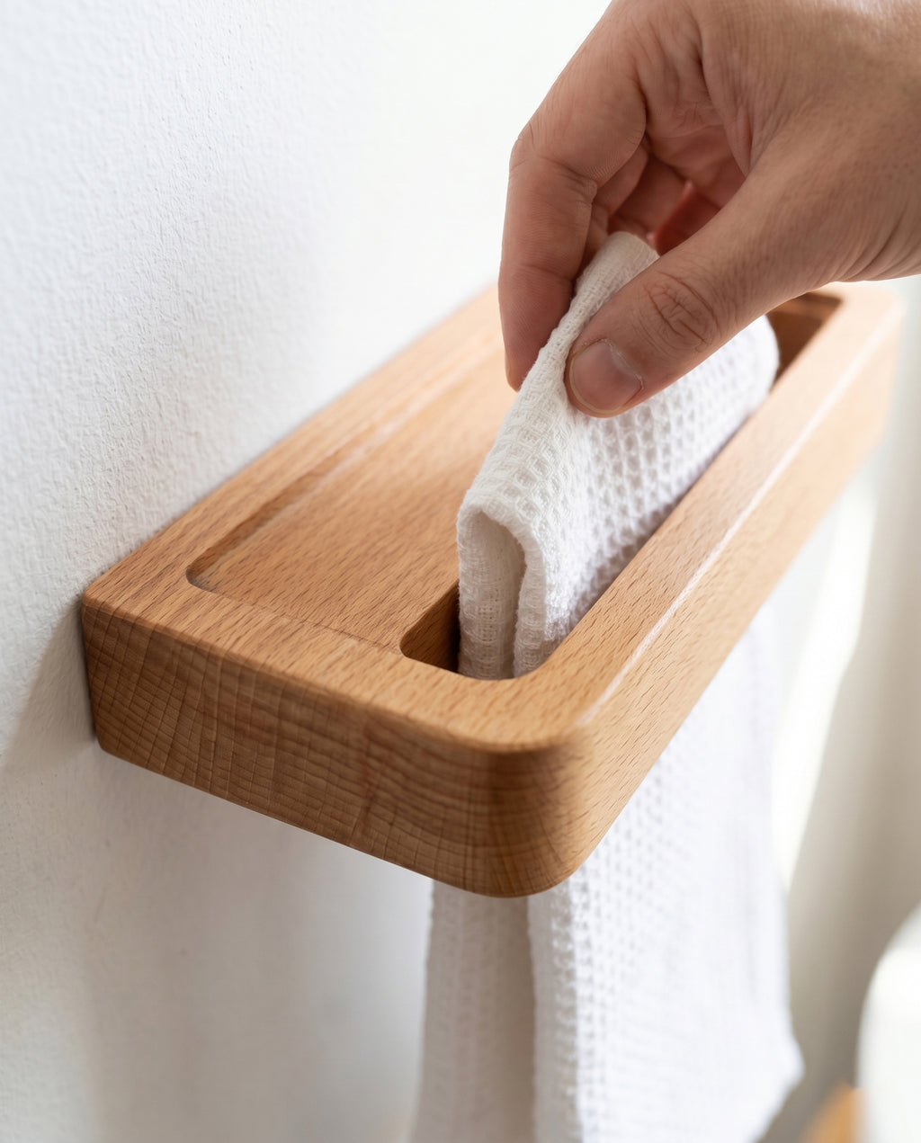 Hand threading white cotton towel down through top slot of wall-mounted Avlia beechwood towel shelf, towel insertion from above, floating shelf design