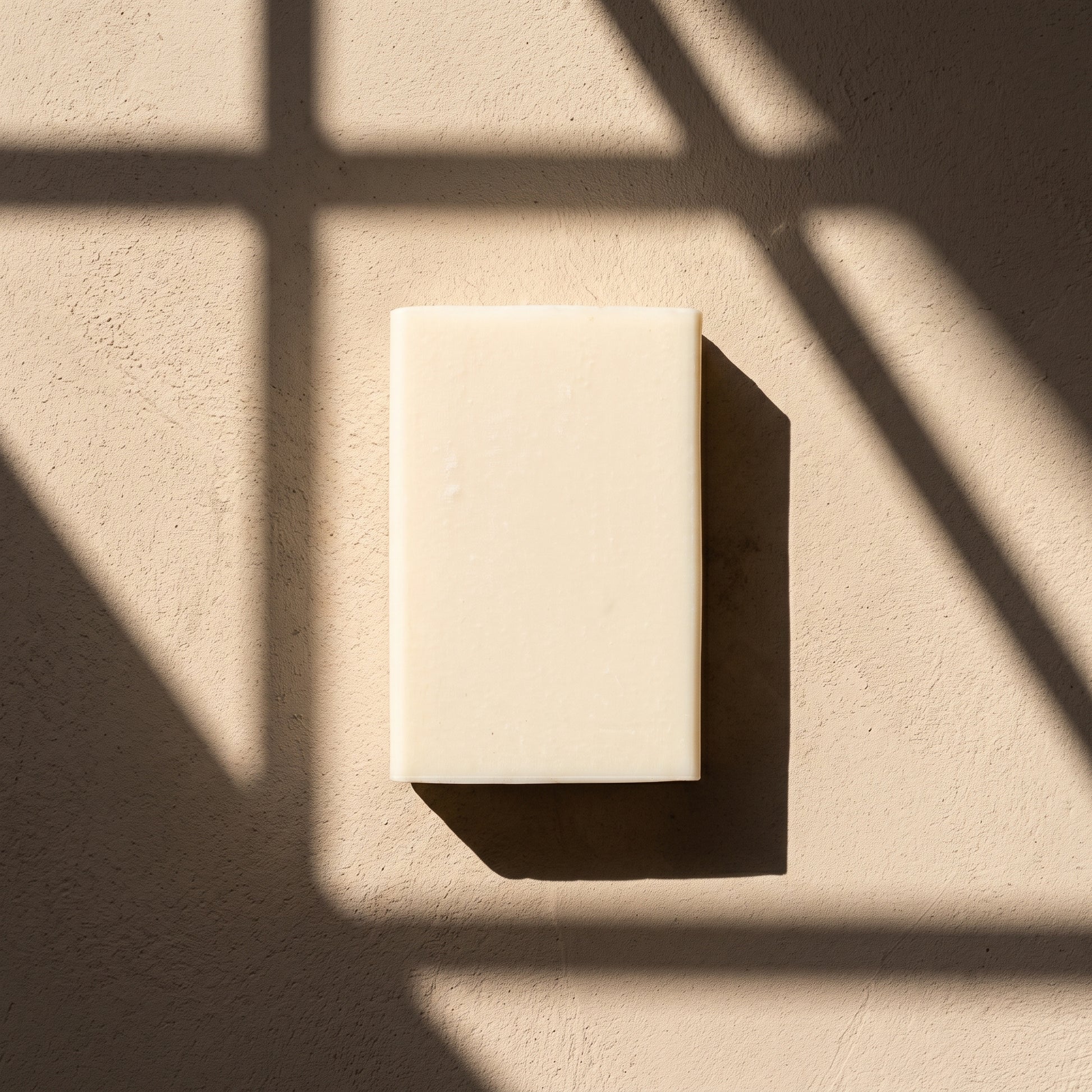 Jasmine Soap Bar in hard afternoon sunlight on sand plaster, cut by geometric window shadows