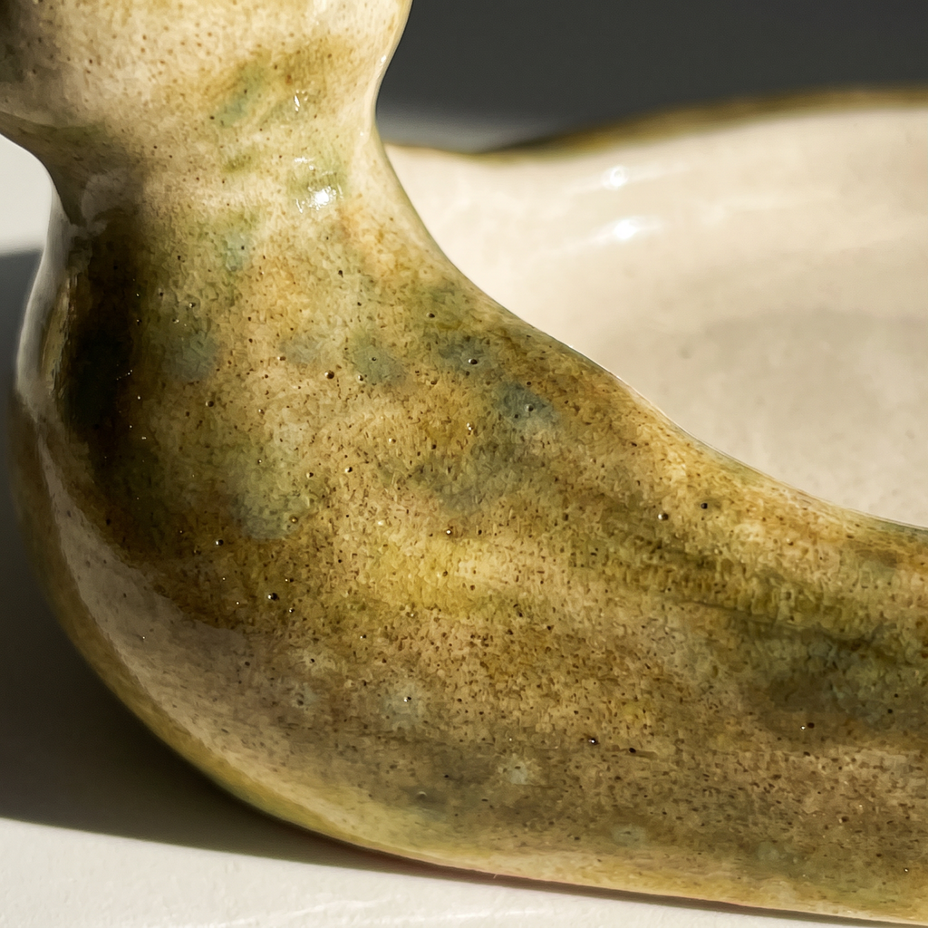 Macro view of the Avlia ceramic duck soap dish glaze, where the mottled green-mustard exterior meets the cream glazed bowl rim