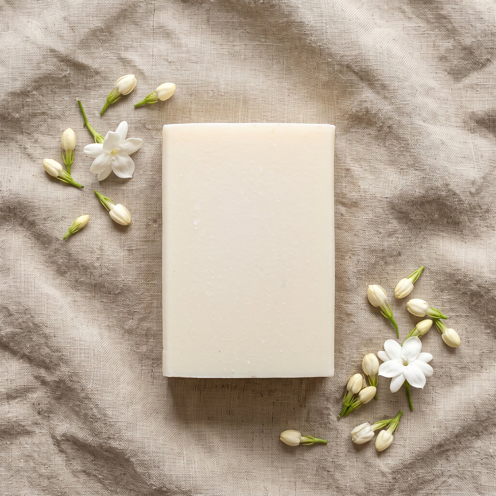 Overhead flat-lay of Jasmine Soap Bar on wrinkled natural linen with fresh jasmine buds and blossoms
