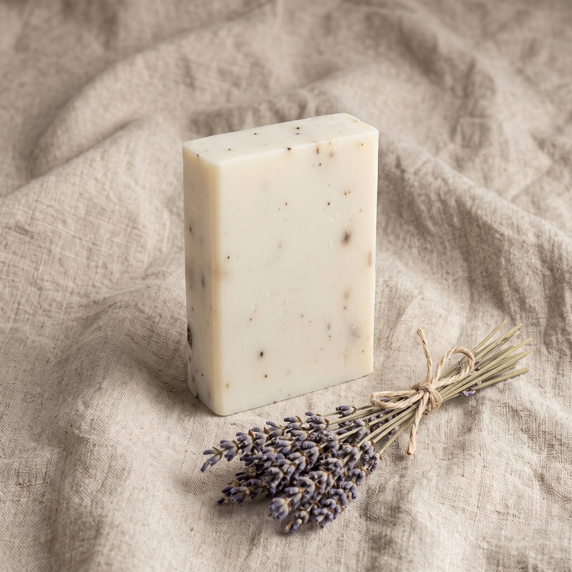 Overhead flat-lay of Lavender Soap Bar on wrinkled natural linen with a tied bundle of dried lavender stems
