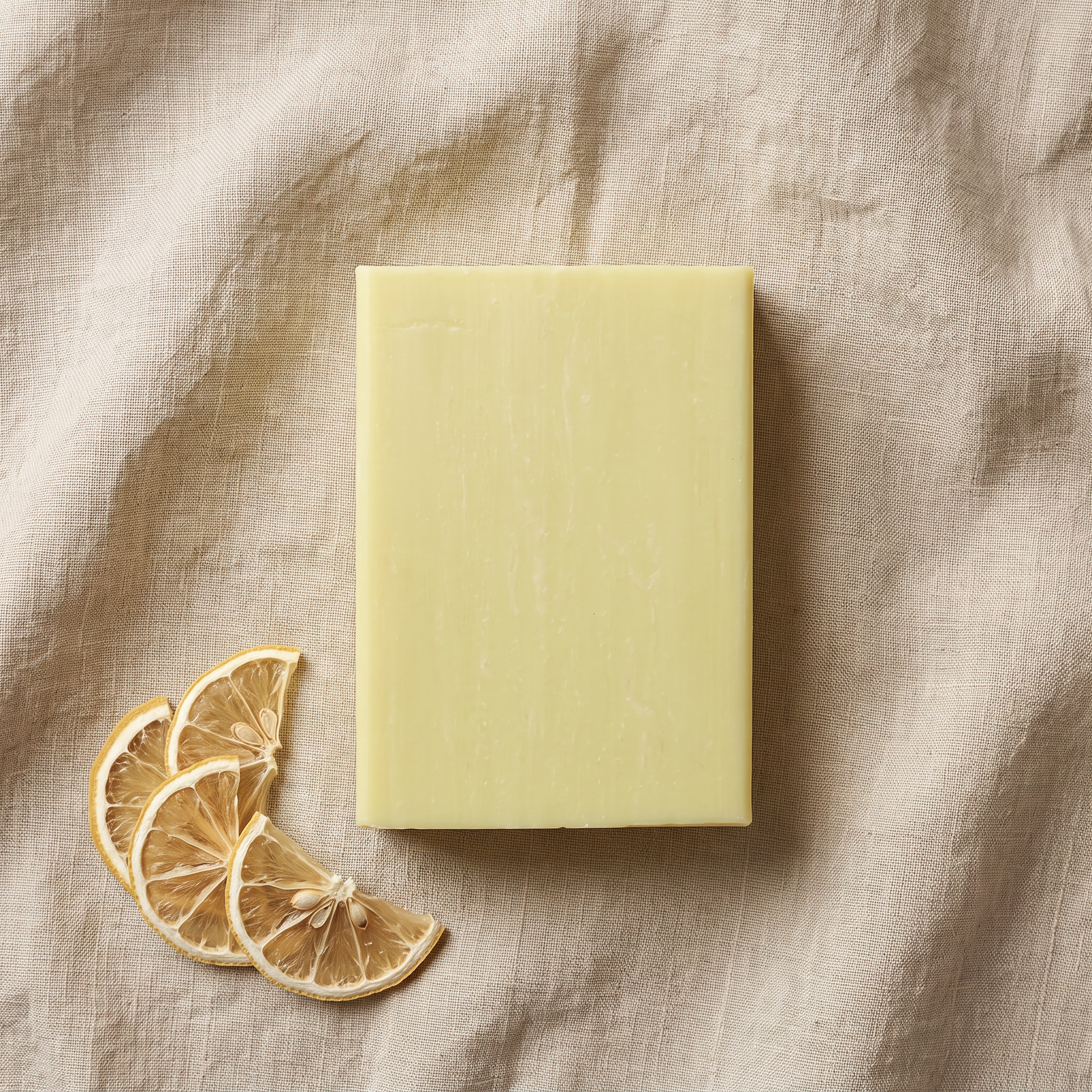 Overhead flat-lay of Lemon Soap Bar on wrinkled natural linen with a fan of dried lemon slices