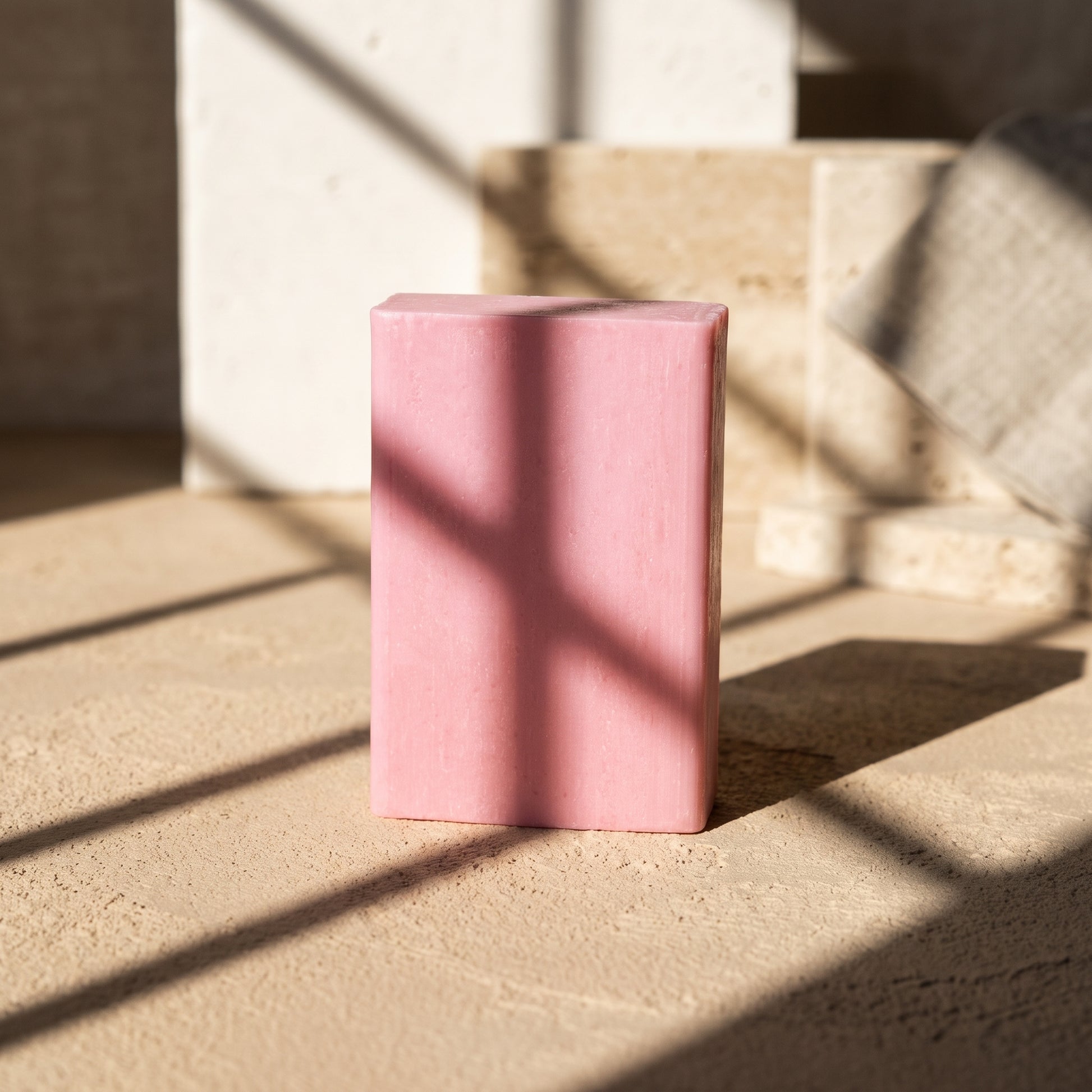 Rose Soap Bar in hard afternoon sunlight on sand plaster, cut by geometric window shadows