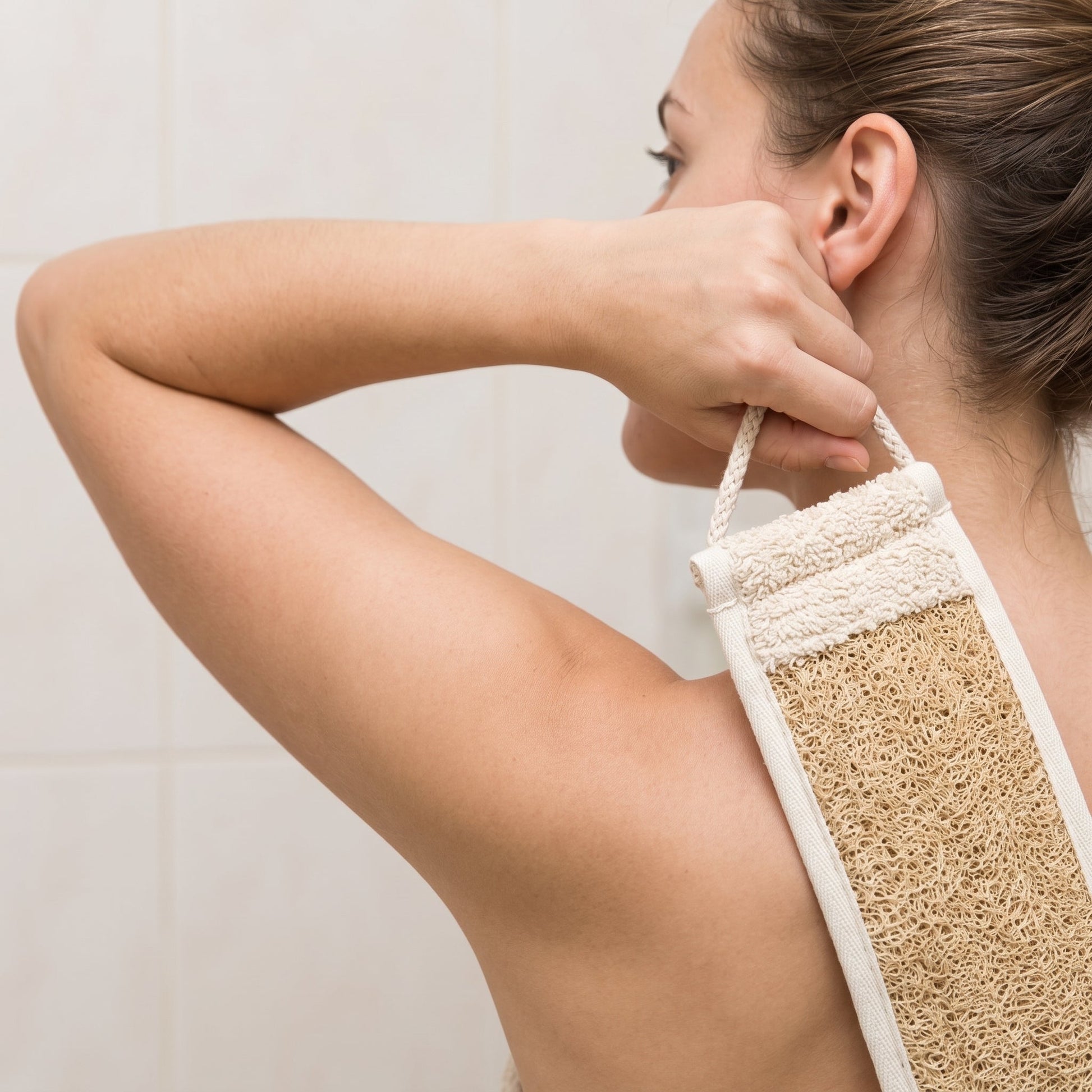 Side view of a woman raising one arm to hold the Avlia luffa strap behind her shoulder, the band running out of view behind her back