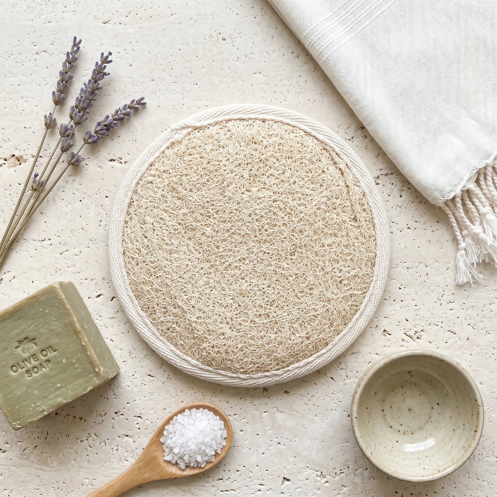 Spa flat lay with round natural loofah pad, olive oil soap, dried lavender and peshtemal towel, eco bath ritual styling