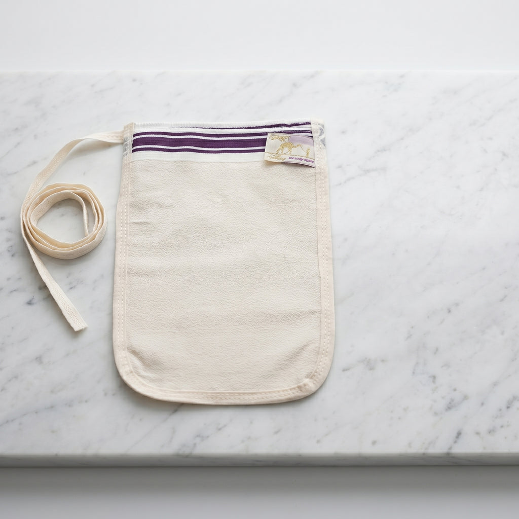 Turkish hammam exfoliating mitt kese made of medium-thickness cream natural off-white crepe fabric lying flat on a polished white Carrara marble slab