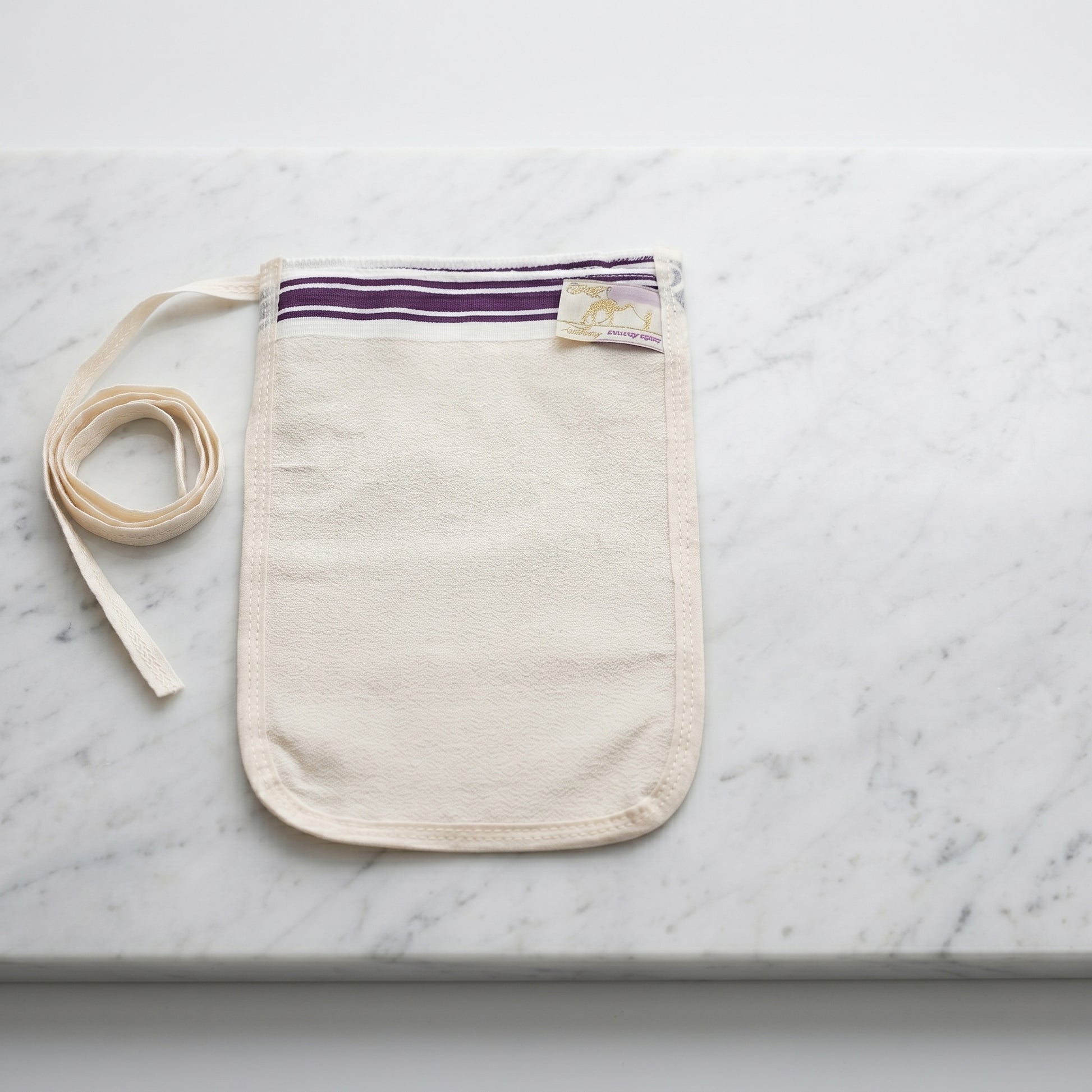 Turkish hammam exfoliating mitt kese made of medium-thickness cream natural off-white crepe fabric lying flat on a polished white Carrara marble slab